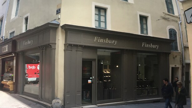 A building with a 'Finsbury' sign, storefronts, and a few pedestrians. - Arena & Maison Carrée (free parking, fully air-conditioned accommodations) (Nîmes)
