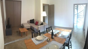A dining area with a wooden table set for four, a sofa, a small coffee table, and a TV in the corner. - Arena & Maison Carrée (free parking, fully air-conditioned accommodations) (Nîmes)