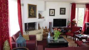 A living room with a TV, red curtains, a sofa, and a coffee table with flowers. - Air-conditioned Provencal villa, 300 m2 garden, quiet location, walking distance to beaches and village (Villeneuve-Loubet)