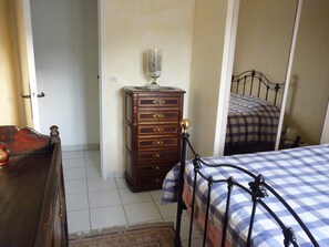 Un dormitorio con un aparador de madera, una cama con colcha a cuadros y un espejo que refleja la cama.