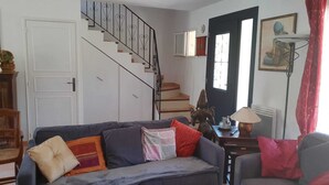 A living room with a staircase, a sofa with cushions, a table with a lamp, and a door with a window. - Air-conditioned Provencal villa, 300 m2 garden, quiet location, walking distance to beaches and village (Villeneuve-Loubet)