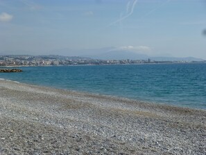 Ein Kiesstrand mit einer Stadtlandschaft im Hintergrund.