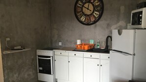 Une cuisine compacte avec des meubles blancs, un four encastré, un four à micro-ondes et une grande horloge murale.