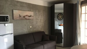 Un salon moderne avec un canapé marron foncé, un réfrigérateur blanc, un four à micro-ondes et un tableau accroché au mur.