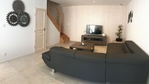 Ein modernes Wohnzimmer mit einer Eckcouch, einem Flachbildfernseher auf einem Holzboden und einer Treppe, die zu einer weiteren Ebene führt.