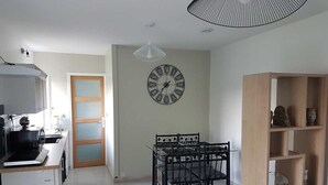 A modern kitchen with a dining area, a clock on the wall, and a ceiling light fixture.