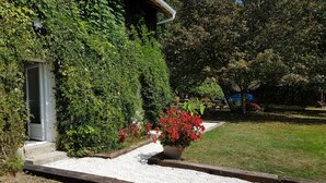 A house with a covered porch, surrounded by dense greenery and a gravel pathway.