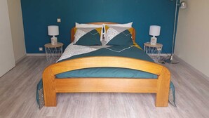 A bedroom with a wooden bed, teal bedding, two bedside tables with lamps, and a blue accent wall.