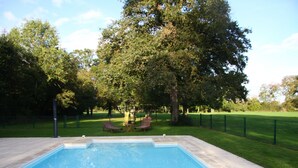 A swimming pool with a tiled deck, surrounded by a grassy area and trees. - Family house in the park with exclusive pool (Vallenay)