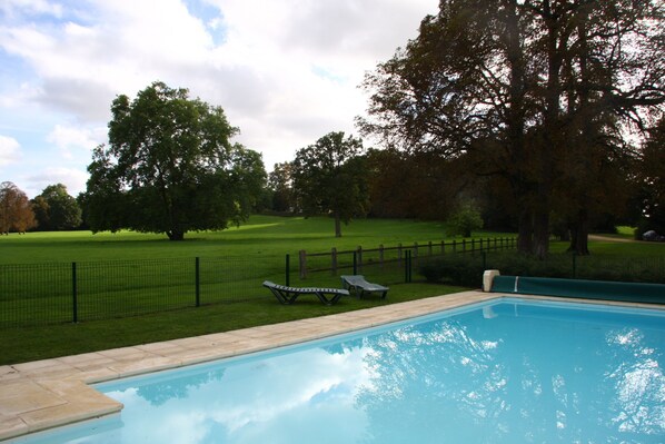 A swimming pool with a wooden deck and lounge chairs, surrounded by a fenced lawn and trees. - Family house in the park with exclusive pool (Vallenay)