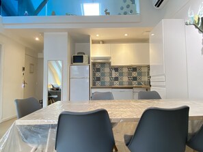 A modern kitchen with white cabinets, a microwave, and a refrigerator. There is a dining table with chairs covered in plastic.