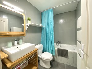 A bathroom with a white sink, toilet, and bathtub. There is a blue shower curtain and a shelf above the sink.