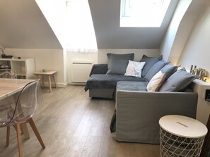 A modern loft apartment with a dining area, a grey sofa set, a small round table, and a radiator.