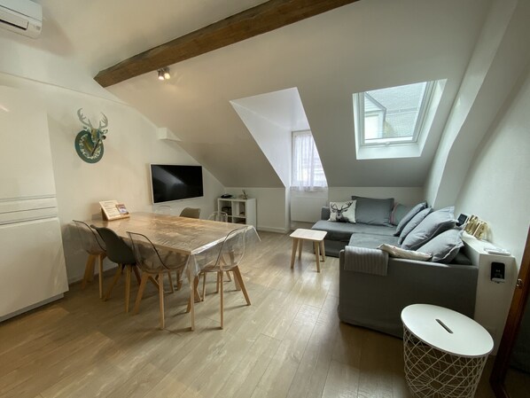 A modern loft apartment with a dining area, a gray sofa, and a TV mounted on the wall.