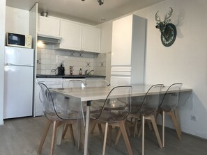 A modern kitchen with white cabinets, a microwave, and a sink. There are four transparent chairs around a table.