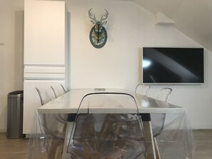 A conference room with a glass table, white walls, a mounted deer head, and a flat-screen TV.