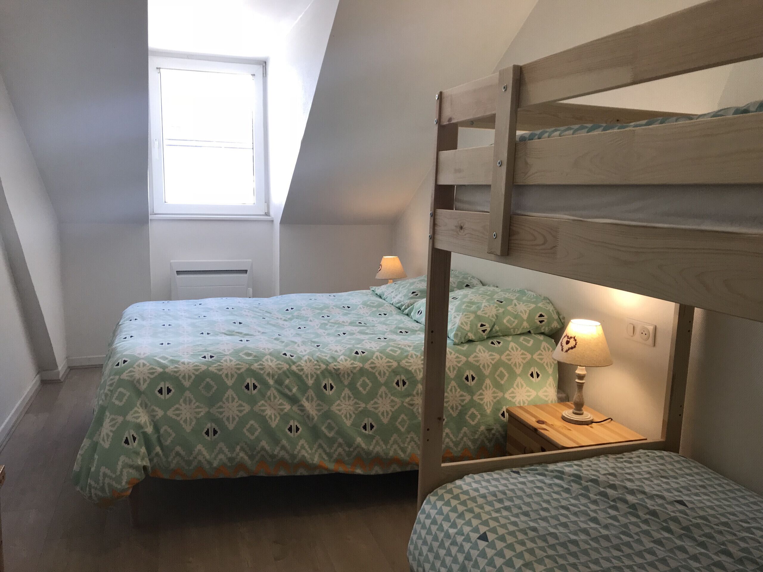 Una habitación con literas, una cama individual, una ventana y una lámpara de noche.