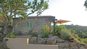 Una casa in pietra con tetto in tegole, area salotto esterna e giardino con rocce e piante.