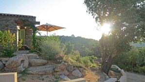 Un edificio in pietra con una porta di legno, un ombrellone all'aperto e un giardino con rocce e piante.