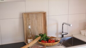 Una cucina con un tagliere di legno, una bottiglia di vino, un cesto di pomodori, una baguette e un piatto di carne.
