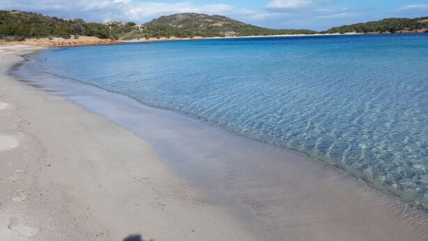 Una spiaggia con acque blu cristalline, una riva sabbiosa e colline in lontananza.