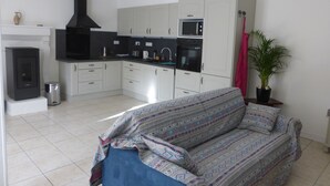 A modern kitchen with white cabinets and black appliances, a sofa with patterned cover, and a potted plant. - Self catering Pont es omnes Pleurtuit (35) (Pleurtuit)