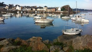A harbor with multiple boats docked, calm water, and a rocky shoreline with buildings in the background. - Self catering Pont es omnes Pleurtuit (35) (Pleurtuit)