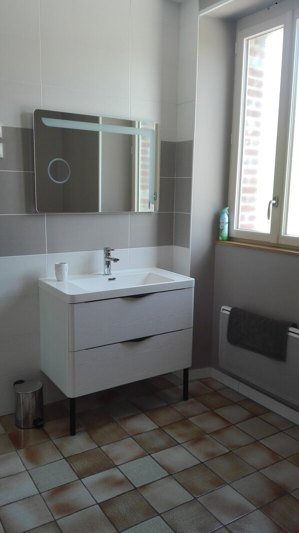 Ein Badezimmer mit weißem Waschtisch, einem Spiegel und einem Fenster.