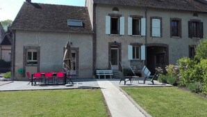 Ein zweistöckiges Gebäude mit einem Ziegeldach, einer kleinen Gartenanlage mit Gartenmöbeln und einem gepflasterten Weg zum Eingang.