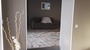 Ein Flur mit einer Blumenvase, einem grauen Sofa im Hintergrund und einem gefliesten Boden.