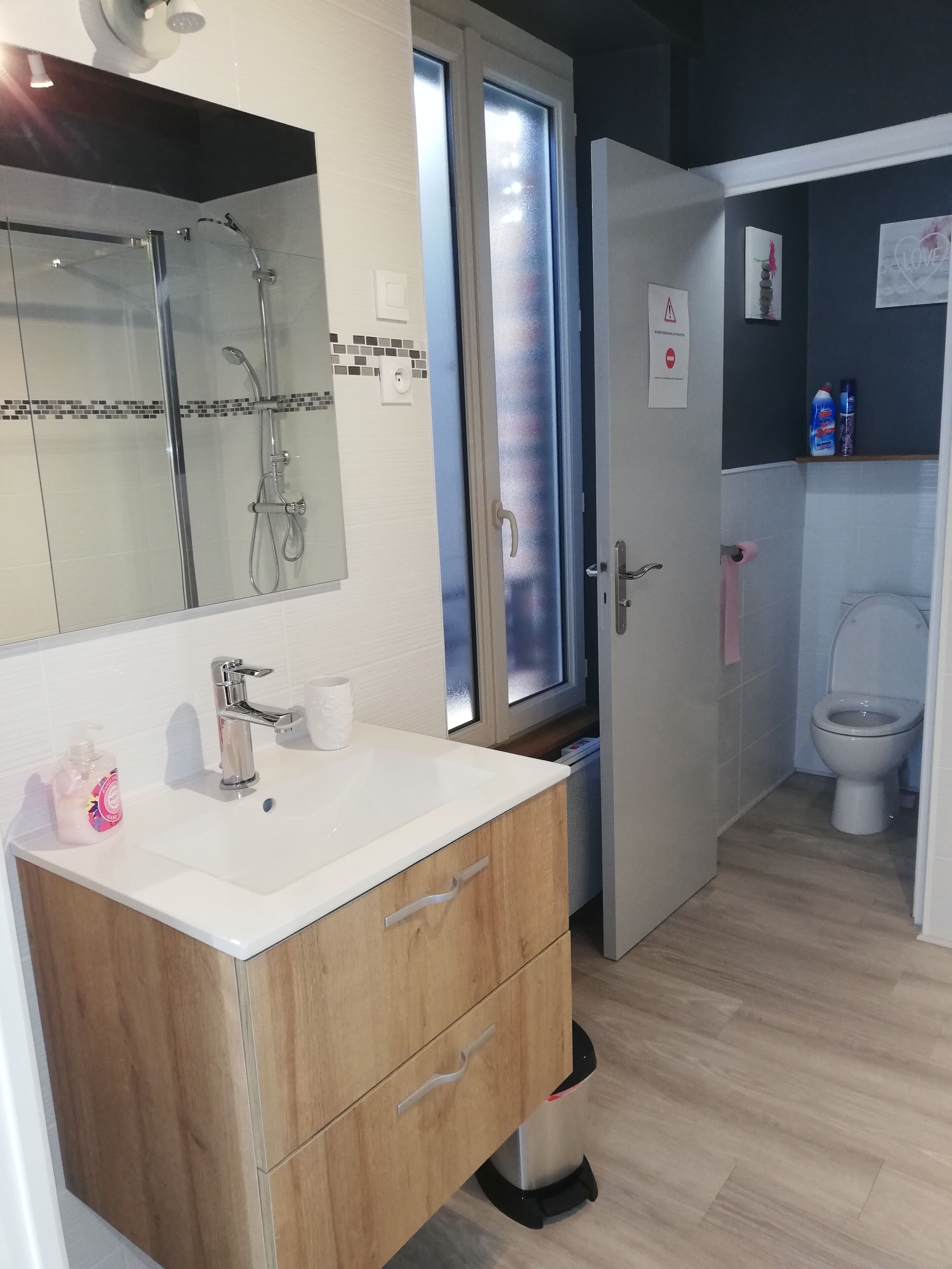 A modern bathroom with a glass shower enclosure, a white sink with a wooden vanity, and a toilet.