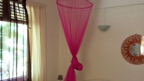 Une chambre à coucher avec un lit, un ventilateur de plafond, une fenêtre avec des rideaux et un miroir fixé au mur.