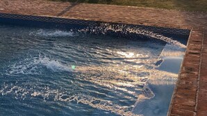 Une piscine bordée de briques, avec une structure en pierre en arrière-plan.