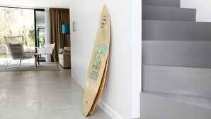 A modern interior with a wooden surfboard leaning against a wall, a staircase, and a seating area with chairs.