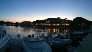 Una marina al crepuscolo con imbarcazioni ormeggiate, acqua calma e un edificio illuminato sullo sfondo.