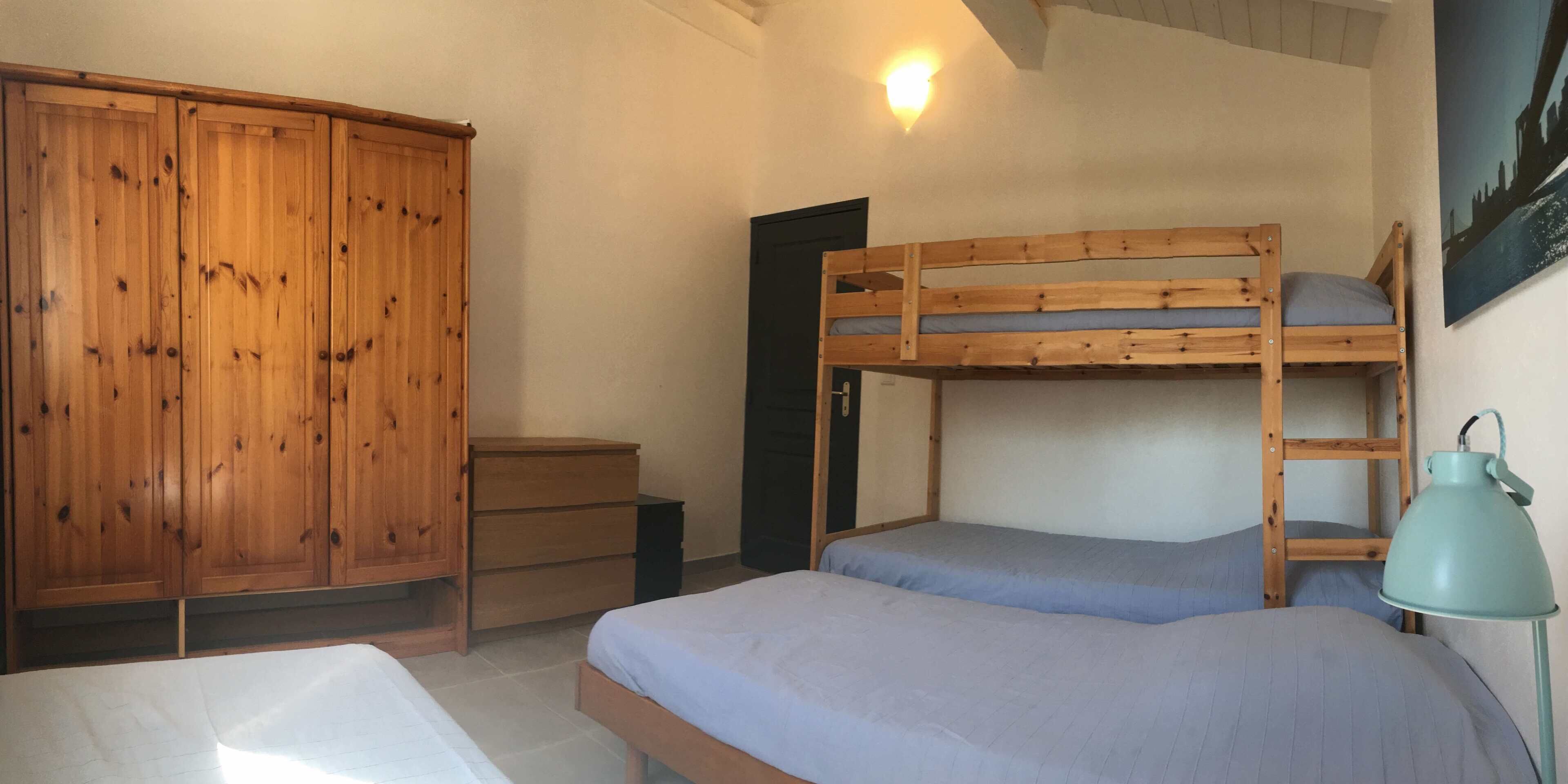 Ein Zimmer mit Etagenbett, Holzschrank, Schreibtisch und Lampe.