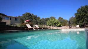 Una piscina trasparente con lettini e una casa sullo sfondo.