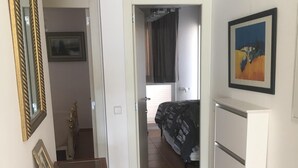 Un pasillo con una mesa de madera, un cuadro enmarco, una cama con edredón estampado y un armario blanco.