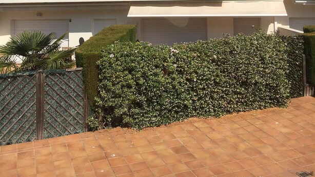 Un edificio residencial de varios pisos con balcones, techo de tejas y un jardín bien cuidado.