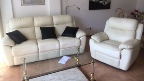 Una sala de estar con un sofá y un sillón color beige, una mesa de centro de vidrio y obras de arte en las paredes.