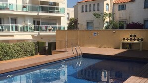Una piscina con cubierta de madera, rodeada de edificios con balcones y tejados de tejas.