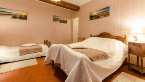 Een hotelkamer met twee bedden, houten hoofdborden, een houten vloer, een witte lamp en twee schilderijen aan de muur.