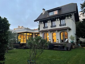 A two-story house with a balcony, large windows, and a well-maintained lawn.