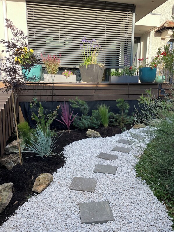 A garden pathway with stepping stones, surrounded by various plants and a modern building with large windows and a slatted awning. - Beautiful house between Paris and Disneyland, sleeps 8, 4 bedrooms - 2 bathrooms (Saint-Maur-Des-Fossés)
