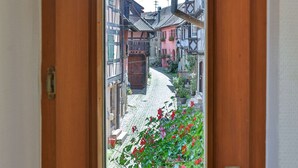 A wooden door with a window view of a cobblestone street lined with traditional buildings.