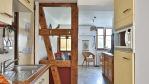A kitchen with a wooden beam structure, a sink, a microwave, and a wicker chair.