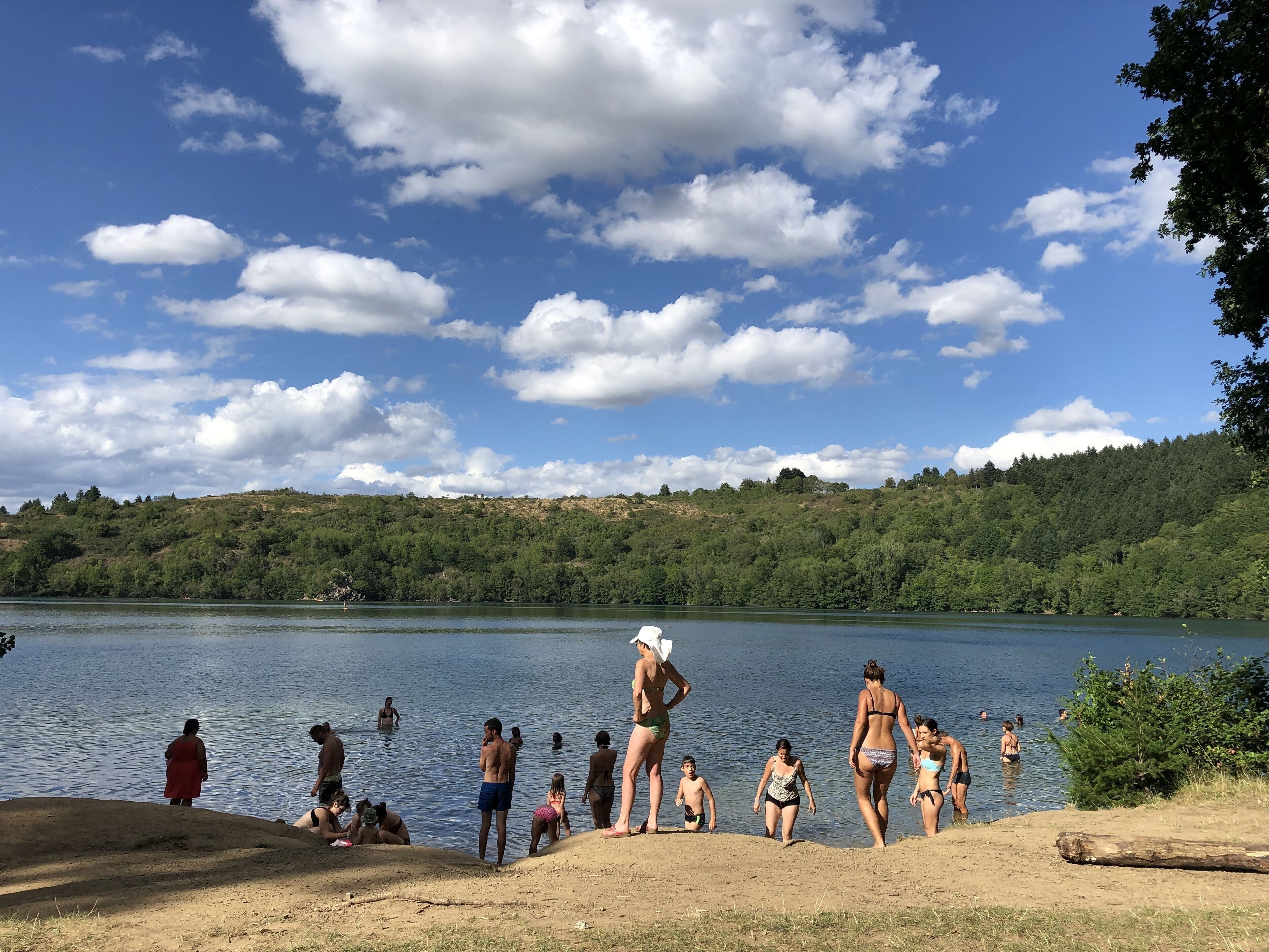 Escena junto a un lago, con gente nadando y de pie en la orilla.