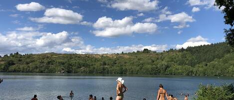 Escena junto a un lago, con gente nadando y de pie en la orilla.