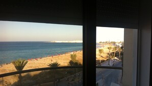 A balcony with a view of a beach, palm trees, and a road with cars.