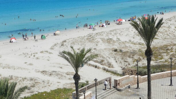 A beach with clear blue water, people swimming, and umbrellas.